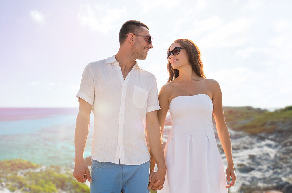 love, people, travel and relations concept - happy couple wearing sunglasses holding hands over summer beach and sea background