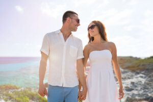 love, people, travel and relations concept - happy couple wearing sunglasses holding hands over summer beach and sea background