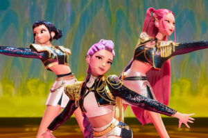 Three animated K-pop idols performing a synchronized dance on stage, wearing glittery futuristic outfits with gold details, from the movie K-Pop Demon Hunters